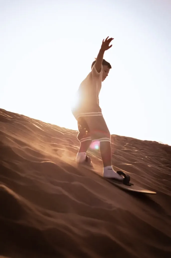 Child sandboarding down a desert dune as part of a family adventure activity.