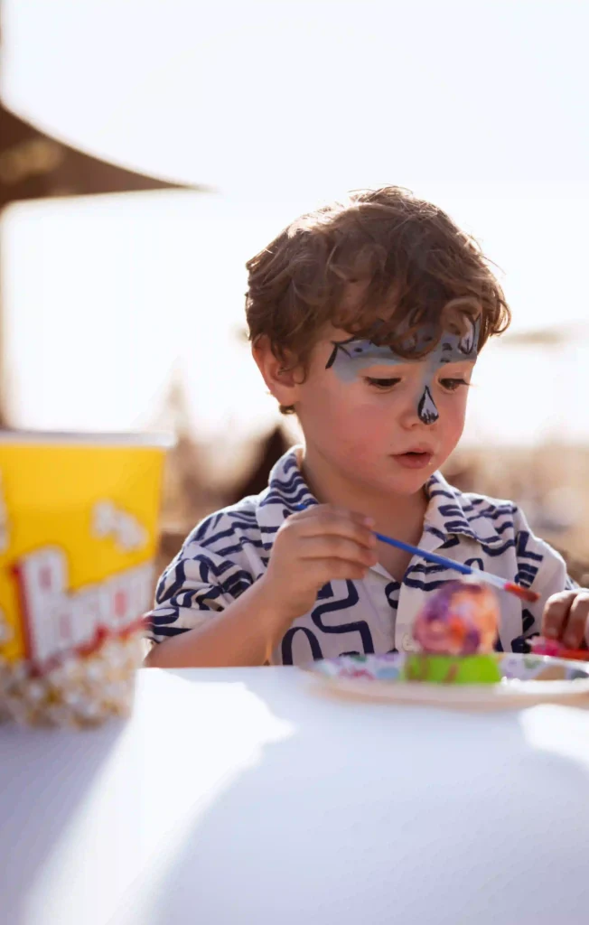 Child with face paint enjoying food at a family friendly desert camp.