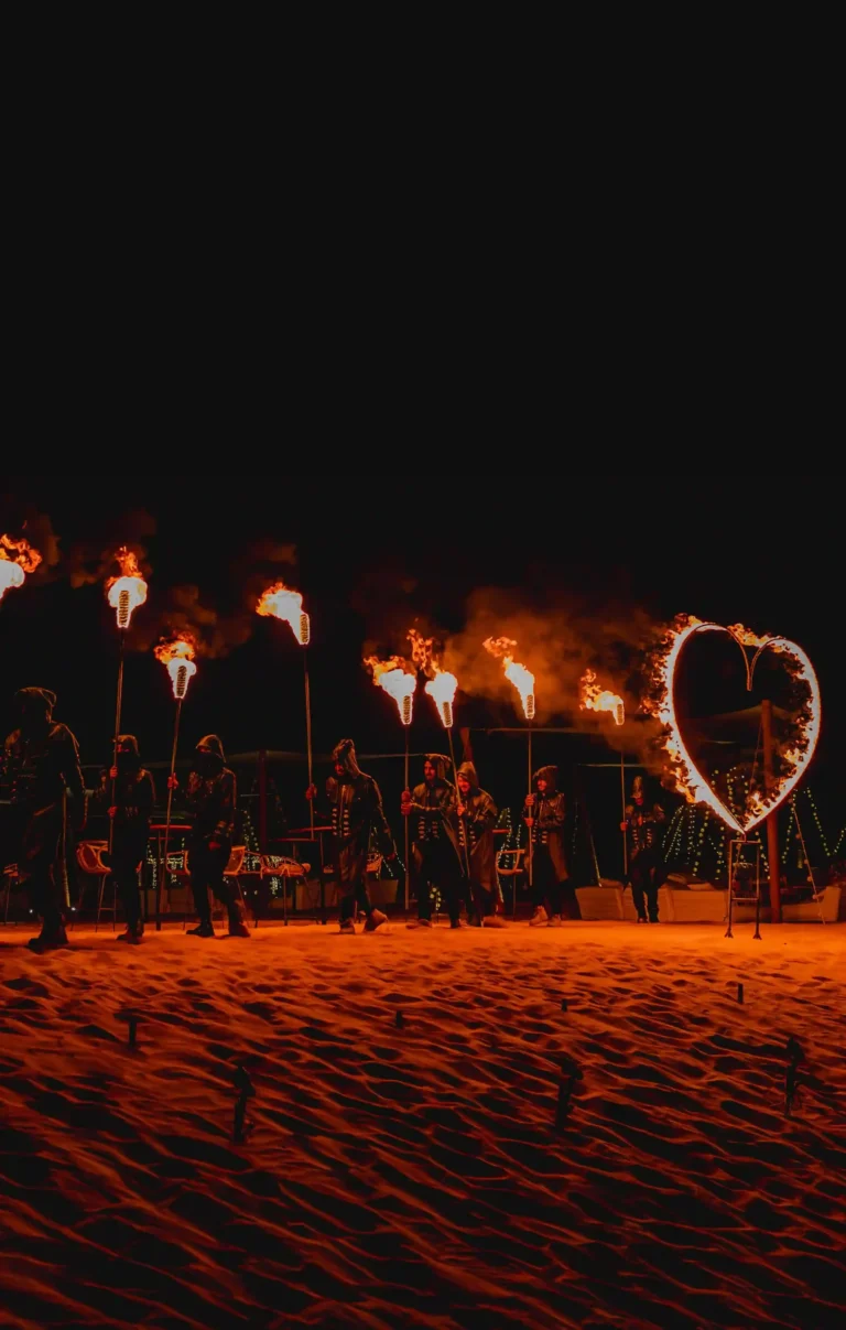 Fire performers forming a heart shape on the sand during a Valentine’s Day evening show.