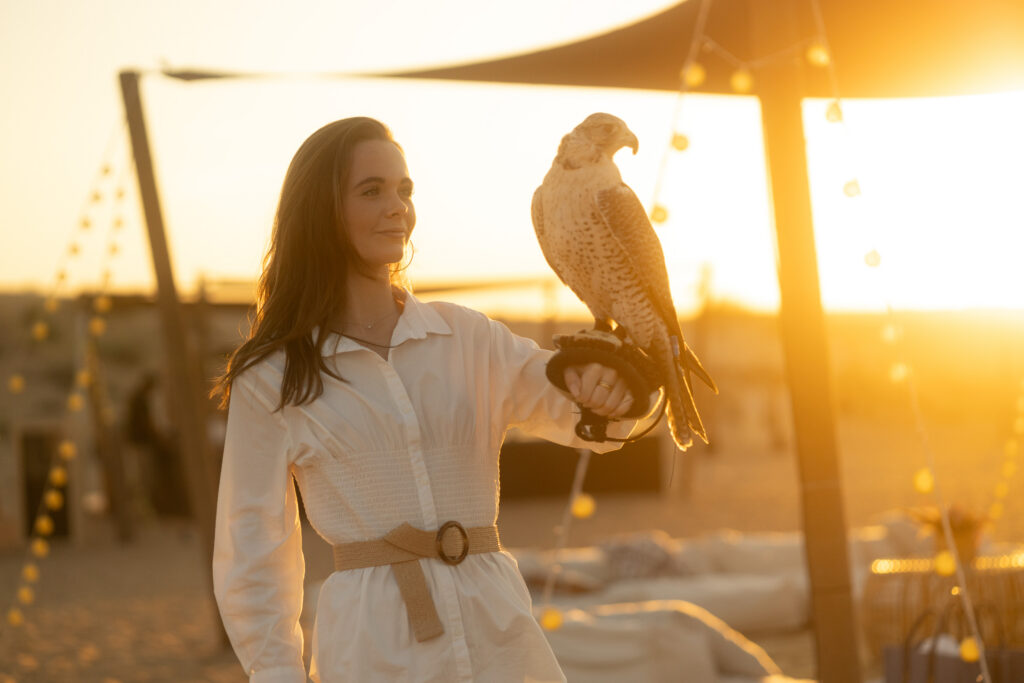 A lady holding a falcon in her arm at sunset, at The Nest in Dubai. 