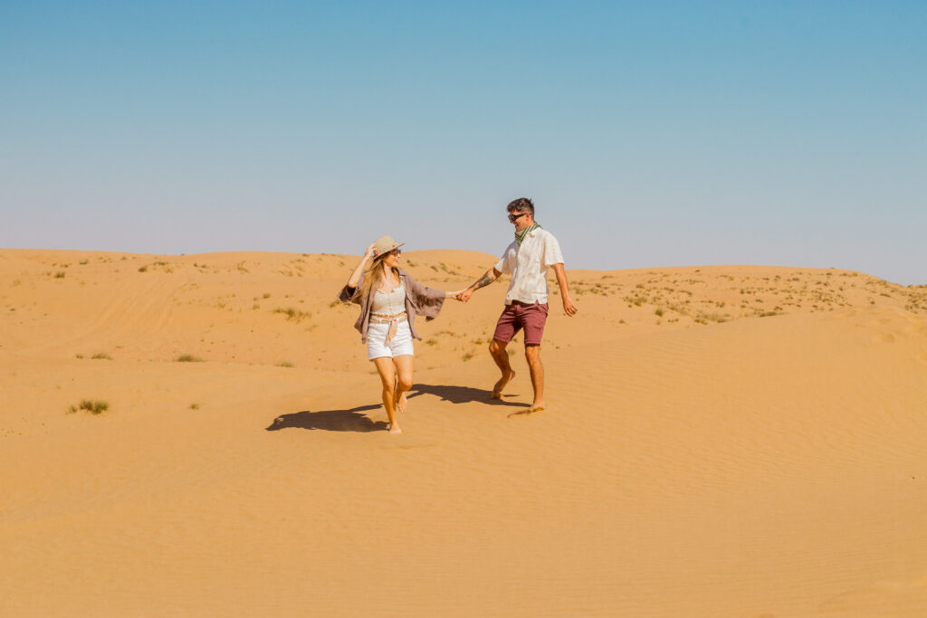A couple walking across the open dunes of the Dubai desert at The Nest by Nara.